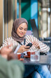 © Jovo Jovanovic/Stocksy - Woman in hijab using phone at outdoor cafe.