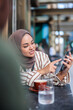 © Jovo Jovanovic/Stocksy - Woman in hijab shows phone at cafe table.