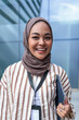 © Jovo Jovanovic/Stocksy - Smiling woman in hijab with ID badge and tablet.