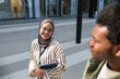© Jovo Jovanovic/Stocksy - Smiling woman in hijab holds tablet, man nearby.
