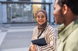 © Jovo Jovanovic/Stocksy - Smiling woman in hijab with tablet talks to friend.