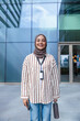 © Jovo Jovanovic/Stocksy - Smiling woman in hijab stands before modern building.