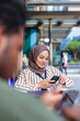 © Jovo Jovanovic/Stocksy - Woman in hijab using phone at outdoor cafe.