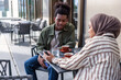 © Jovo Jovanovic/Stocksy - Young couple at outdoor cafe, looking at phone.