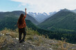 © SHOTPRIME STUDIO - A lone hiker stands on a rocky ledge, back to camera, raising an arm as distant mountains rise, capturing a sweeping outdoor landscape filled with adventure