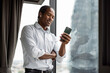 © Maia Images/Stocksy - Happy American Man in Business Casual, Using Smartphone by Window