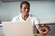© Maia Images/Stocksy - Professional Black Man Working On Laptop At Desk Holding Card