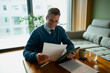 © Artcore Studio/Stocksy - Mature man smiling while reading document at home office