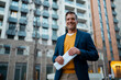 © Artcore Studio/Stocksy - Confident man smiling outdoors holding documents in urban setting