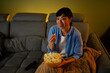 © Artcore Studio/Stocksy - Woman watching television and eating popcorn on sofa