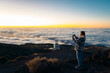 © Santi Nuñez/Stocksy - Woman capturing mountain sunset above clouds with phone