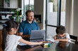 © NZstockphoto - Children draw and colour as their father works on a laptop in a stylish home setting.