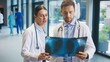 © VAKSMANV - Two focused doctors standing in bright clinic hallway studying chest X-ray together. Female colleague pointing at detail while male doctor examining image closely. Professionals reviewing findings.