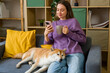 © Westend61 - Relaxed woman enjoying coffee and smartphone with dog in cozy living room