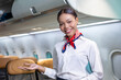 © Akarawut - African flight attendant posing with smile face at middle of the aisle inside aircraft for welcoming passenger on board with seat on background