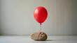 © olgakris - Red balloon tied to heavy rock concept illustrating contrast between lightness and weight, limitation versus freedom, resilience, emotional burden, inner strength, mental health and perseverance