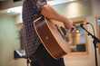 © Wavebreak Media - Male musician in dark plaid shirt playing acoustic guitar by mic stand, console and studio window