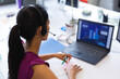 © Wavebreak Media - Asian woman sitting at office desk wearing purple blouse and headset and analyzing charts on laptop