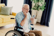 © deagreez - Elderly man in wheelchair uses smartphone at home in a bright living room, exploring technology and daily life