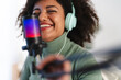 © Studio Marmellata - A woman with curly hair wears headphones and smiles while speaking into a microphone with colorful lights.