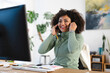 © Studio Marmellata - A smiling woman with curly hair adjusts her headset while working at her desk, looking at a computer screen.