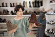 © JackF - Female customer is standing next to shelf in stores sales area. She picks up shoes, looks at and studies material and quality of product, decides to buy shoes
