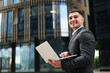 © muse studio - Businessman using laptop outside modern building
