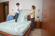 © dargog - Mother and son making the bed together in a bright bedroom, teaching responsibility and teamwork while sharing domestic chores, smiling and bonding during a cozy morning routine