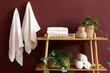 © Pixel-Shot - Shelf unit with clean towels and plants near burgundy wall in room