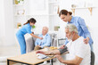 © New Africa - Woman playing dominoes with senior man at table and care worker helping her patient at retirement home, selective focus