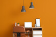 © Pixel-Shot - Workplace with blank laptop and lamps near orange wall