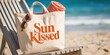 © Ross - Sun kissed beach tote bag on lounge chair with sunglasses and towel on sandy shore against turquoise ocean summer vacation concept