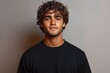 © btiger - Young man with curly hair in a black crew neck t-shirt against a plain gray studio backdrop, calm neutral mood, minimalist head and shoulders portrait