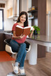 © Fahng - Pretty young woman with cup of coffee or tea reading book in modern kitchen counter at home apartment.  Morning lifestyle concept.