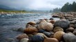 © Thares2020 - Close up of wet river pebbles on a rocky bank with a flowing stream and misty mountains in the background