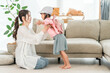 © buritora - A mother helps her daughter get dressed in the living room at home