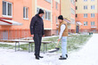 © Nadya Kolobova - Two men shoveling snow in a residential area. One is a young Asian man wearing a brown vest, and the other is a senior Caucasian man in a black coat.