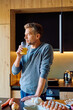 © we.bond.creations - Man enjoying a healthy morning drink of orange juice, preparing a meal with fresh ingredients in a stylish kitchen