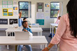 © Wavebreak Media - Students and teacher engaging in classroom as African American youth male raising hand using laptop