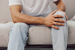 © SHOTPRIME STUDIO - Young man sitting on a sofa, displaying a thoughtful expression while holding his knee. Warm tones and cozy decor create a relaxed atmosphere.