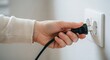 © ALLmost - A person's hand is seen plugging a black electrical cord into a white wall power outlet, connecting a device to electricity.