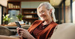 © peopleimages.com - Old woman, phone and laugh on couch with texting, notification and funny chat in living room at house. Person, smartphone and happy with mobile app, contact and social network on sofa at apartment