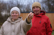 © sementsova321 - Two people stand outside in winter clothes, holding house keys. They are near a wooden structure and the sky is cloudy