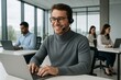 © diproduction - Smiling male customer support agent with headset working on laptop in modern office with team in background, showing teamwork and communication concept. Ai generative