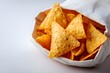 © Anuson - Triangle corn tortilla chips spilling out of a light s bag on a white surface ready to be served as snack or party appetizers.