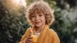 © liliyabatyrova - Curly-haired child delights in a glass of vibrant orange juice, wearing a cozy yellow robe. Bright sunlight filters through leafy greenery, creating a joyful scene