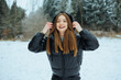 © DSMT - Woman with long hair wearing black coat standing in snowy landscape and smiling while holding her hood during winter season