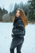 © DSMT - Woman stands in snowy field wearing a black jacket and pants while trees are in the background on a cold winter day