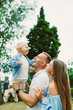 © DSMT - Family enjoys a sunny day at the park while a father lifts his smiling child into the air as the mother watches with joy