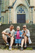 © DSMT - Family sits on steps of a building while using mobile phones on a sunny day